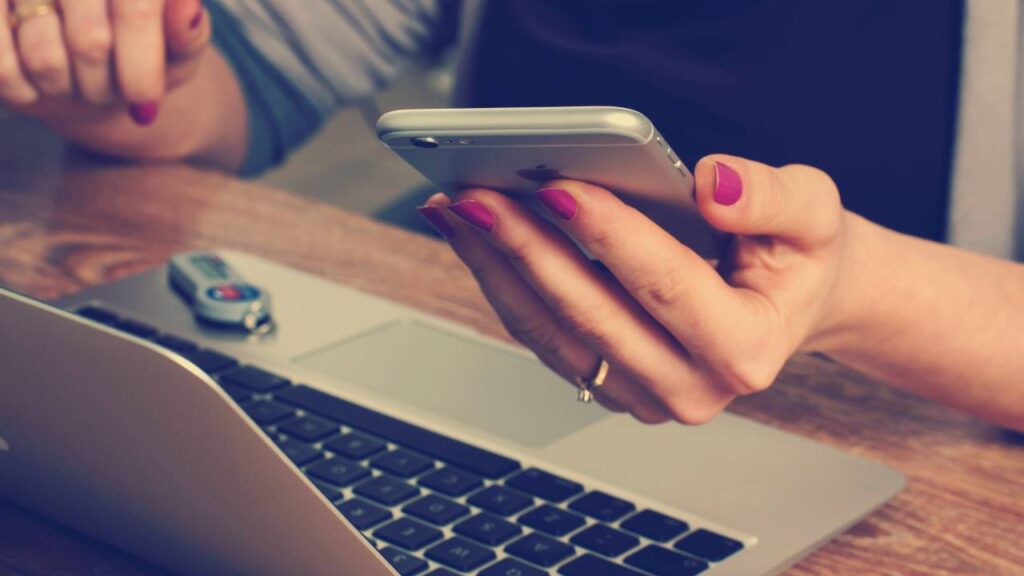 A woman holding an iPhone above her laptop