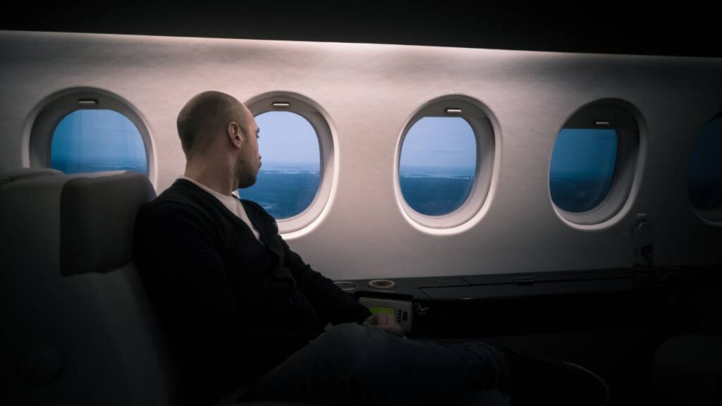 A bald man staring at the landscape through the window of an airplane