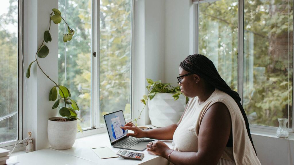 Woman working on a laptop next to large windows