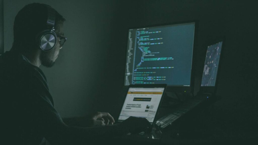 A photo of a man using several computers at once in the dark