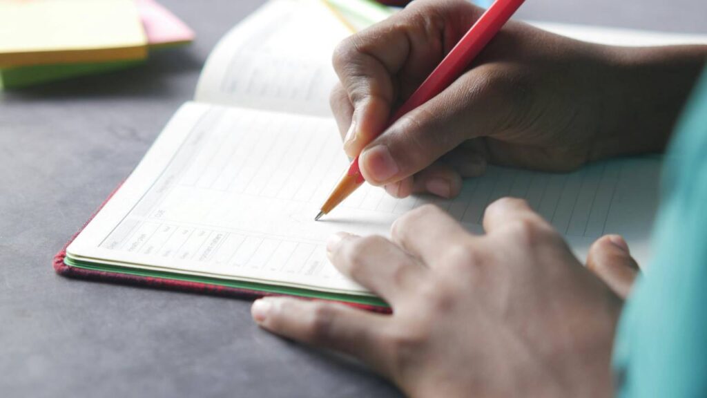 A person using a pen to write in the notebook