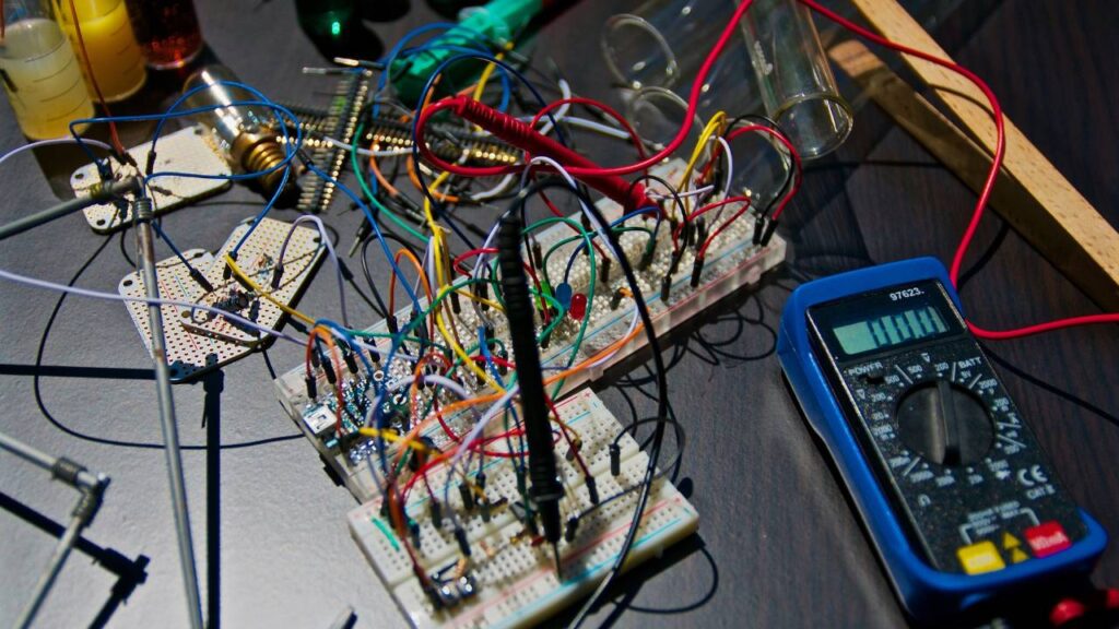 A multimeter placed next to several electrical components full of colourful wires